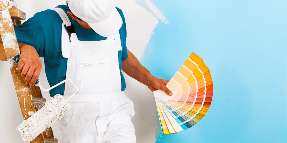 portrait of painter man with paintroller and wooden vintage ladder showing a color palette, on half painted wall